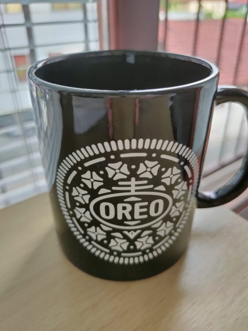 A black coffee mug with a white Oreo logo printed on it.